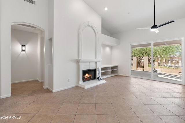 unfurnished living room featuring ceiling fan, light tile patterned floors, high vaulted ceiling, and a tiled fireplace