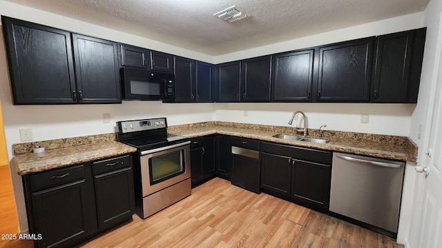 kitchen featuring stainless steel appliances, sink, a textured ceiling, stone counters, and light wood-type flooring