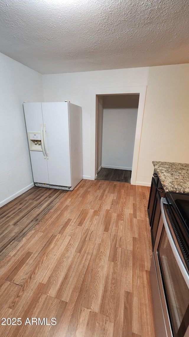 interior space with a textured ceiling, white refrigerator with ice dispenser, stainless steel electric stove, and light stone counters