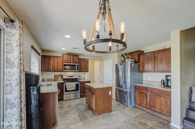 kitchen with an inviting chandelier, a kitchen island, visible vents, appliances with stainless steel finishes, and a sink