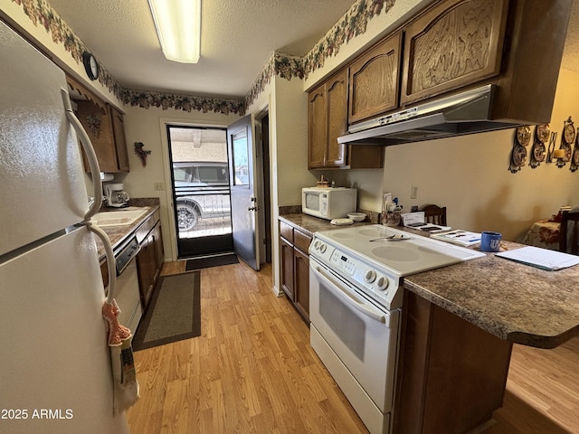 kitchen with a breakfast bar, dark brown cabinets, white appliances, a textured ceiling, and light hardwood / wood-style flooring