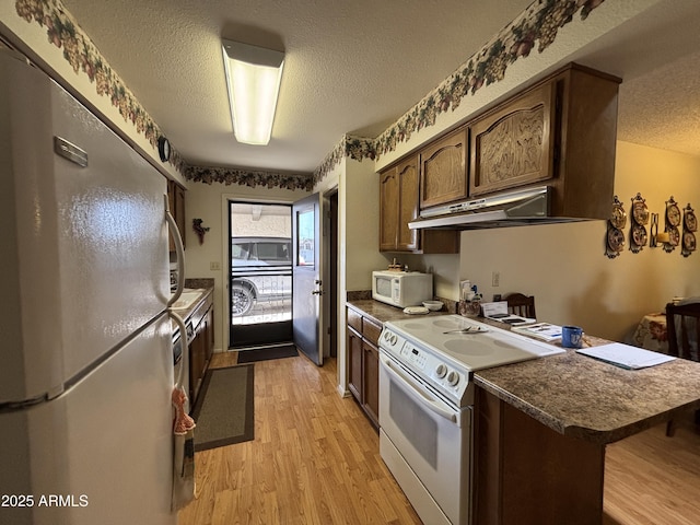 kitchen with kitchen peninsula, a kitchen breakfast bar, light wood-type flooring, a textured ceiling, and white appliances