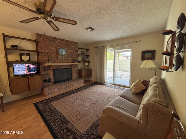 living room with a brick fireplace, ceiling fan, a textured ceiling, and light hardwood / wood-style flooring