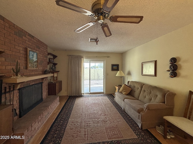 living room with ceiling fan, a textured ceiling, and a brick fireplace