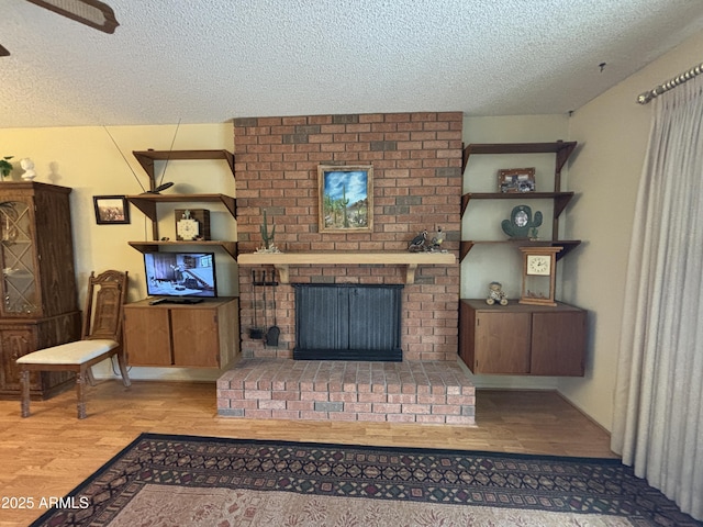 living room with a brick fireplace, a textured ceiling, and light hardwood / wood-style flooring