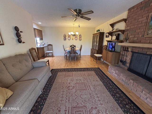 living room featuring a fireplace, a textured ceiling, light hardwood / wood-style floors, and ceiling fan with notable chandelier