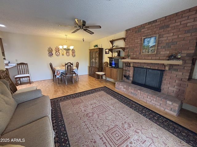 living room featuring ceiling fan with notable chandelier, a textured ceiling, light hardwood / wood-style floors, and a brick fireplace