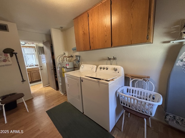 washroom featuring cabinets, light wood-type flooring, washing machine and dryer, and water heater