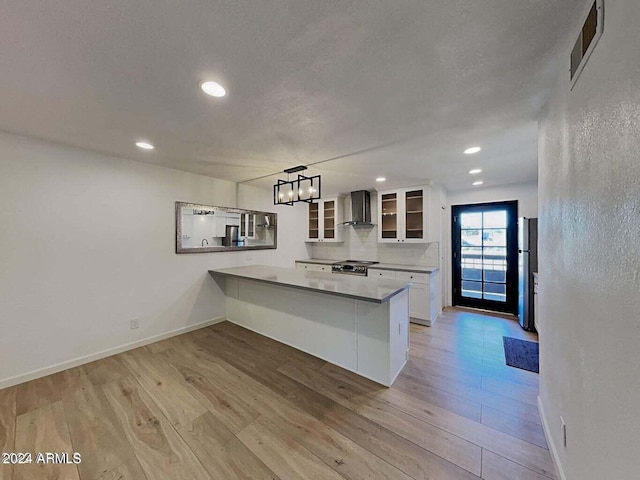 kitchen with pendant lighting, wall chimney range hood, white cabinetry, and light hardwood / wood-style floors