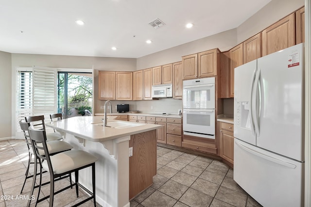 kitchen featuring sink, white appliances, an island with sink, a breakfast bar area, and light tile patterned floors