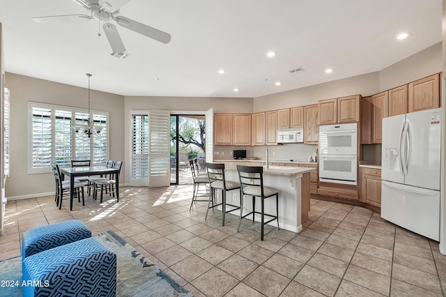 kitchen with pendant lighting, a wealth of natural light, white appliances, a kitchen island with sink, and light tile patterned flooring