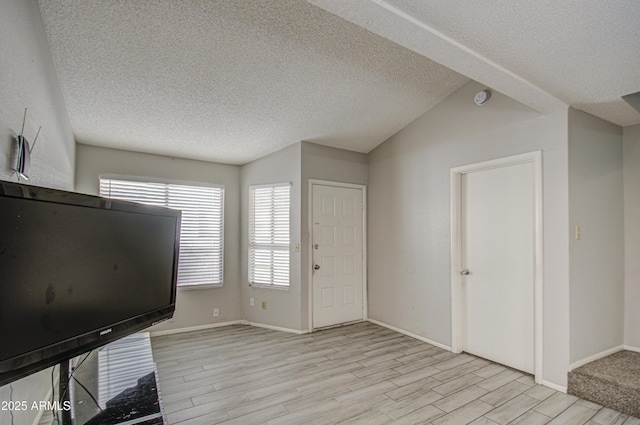 entrance foyer with light hardwood / wood-style floors, a textured ceiling, and lofted ceiling