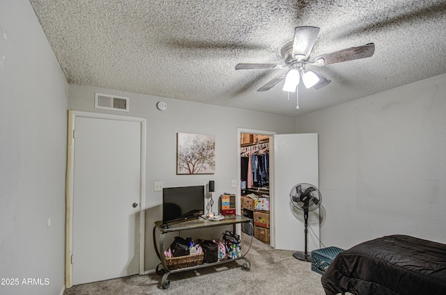 bedroom with ceiling fan, light colored carpet, a textured ceiling, a walk in closet, and a closet