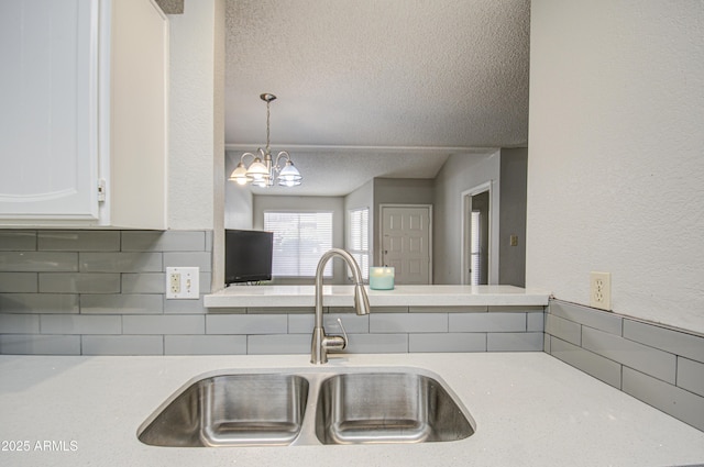 kitchen with tasteful backsplash, hanging light fixtures, a textured ceiling, white cabinets, and sink