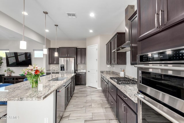 kitchen with decorative light fixtures, sink, a kitchen island with sink, light stone counters, and stainless steel appliances