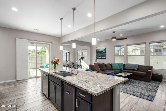 kitchen with pendant lighting, sink, stainless steel dishwasher, light stone counters, and a center island with sink