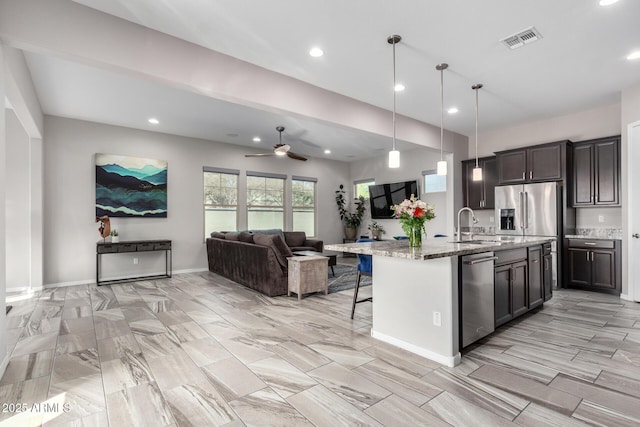 kitchen with pendant lighting, stainless steel appliances, light stone counters, an island with sink, and a kitchen bar