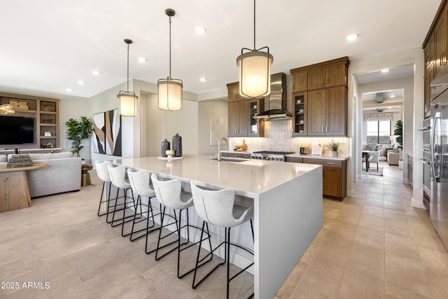 kitchen with a spacious island, wall chimney exhaust hood, open floor plan, decorative light fixtures, and light countertops