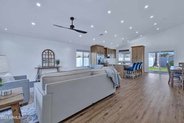 living room featuring ceiling fan, high vaulted ceiling, and light hardwood / wood-style flooring