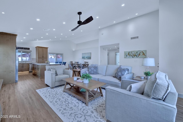 living room featuring ceiling fan, high vaulted ceiling, and light hardwood / wood-style flooring