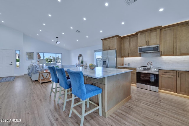 kitchen with stainless steel appliances, a kitchen breakfast bar, light stone counters, a center island with sink, and light wood-type flooring