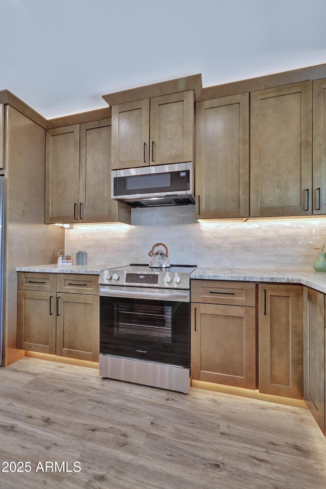 kitchen featuring extractor fan, tasteful backsplash, light hardwood / wood-style floors, stainless steel appliances, and light stone countertops