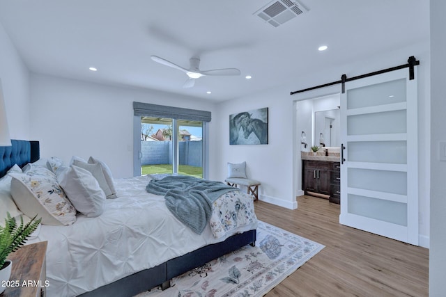 bedroom featuring ceiling fan, access to exterior, connected bathroom, light hardwood / wood-style floors, and a barn door