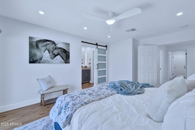 bedroom with ceiling fan, a barn door, hardwood / wood-style floors, and ensuite bath