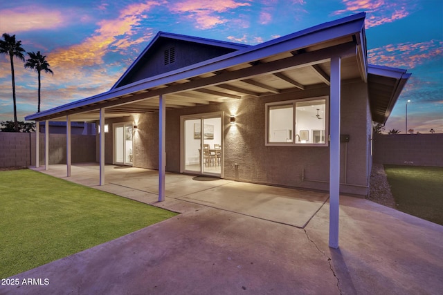 back house at dusk with a patio area and a lawn