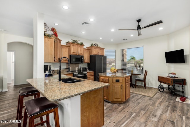 11312 E Newcastle Ave, Mesa, AZ 85209 - kitchen with black appliances, arched walkways, a kitchen island, light stone counters, and a kitchen breakfast bar