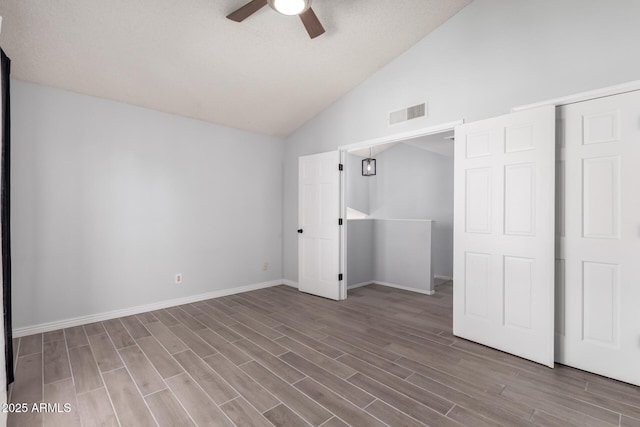 unfurnished bedroom featuring ceiling fan, lofted ceiling, a barn door, and wood-type flooring