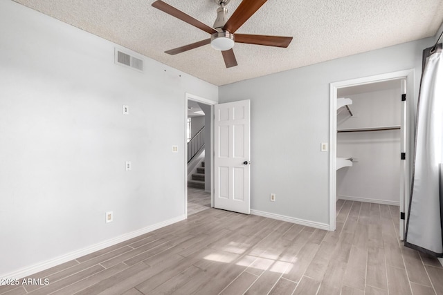 unfurnished bedroom featuring ceiling fan, a spacious closet, light hardwood / wood-style floors, and a textured ceiling