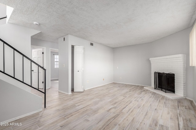 unfurnished living room with a brick fireplace, a textured ceiling, and light hardwood / wood-style flooring