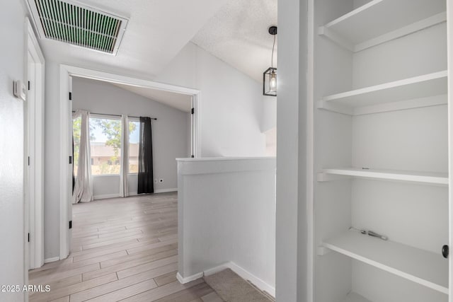 hall featuring lofted ceiling, a textured ceiling, and light hardwood / wood-style flooring