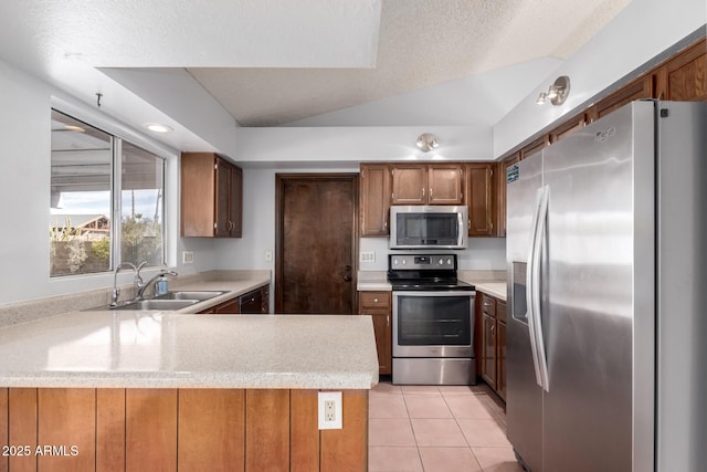 kitchen featuring vaulted ceiling, appliances with stainless steel finishes, sink, light tile patterned floors, and kitchen peninsula