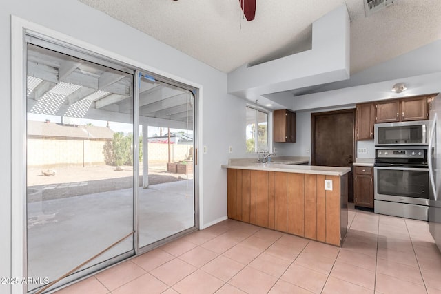 kitchen with lofted ceiling, sink, light tile patterned floors, kitchen peninsula, and stainless steel appliances