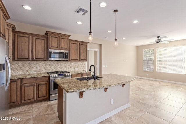 kitchen with sink, decorative light fixtures, appliances with stainless steel finishes, a kitchen breakfast bar, and an island with sink