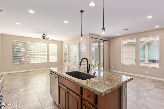 kitchen featuring sink, light stone counters, decorative light fixtures, stainless steel dishwasher, and a kitchen island with sink