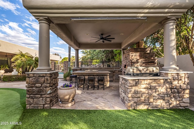 view of patio featuring area for grilling, ceiling fan, an outdoor kitchen, exterior bar, and an outdoor stone fireplace