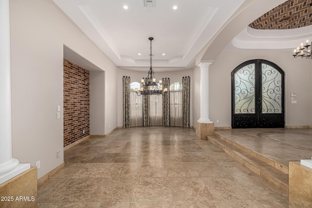 entryway featuring ornate columns, a chandelier, a raised ceiling, and french doors