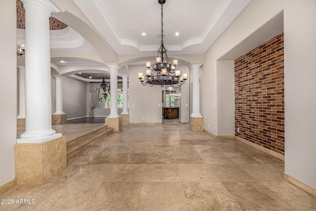 interior space featuring decorative columns, brick wall, a raised ceiling, and an inviting chandelier