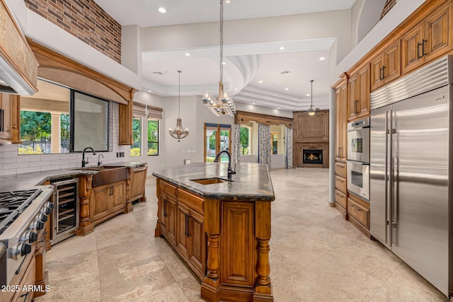 kitchen with an island with sink, a large fireplace, beverage cooler, hanging light fixtures, and high end appliances