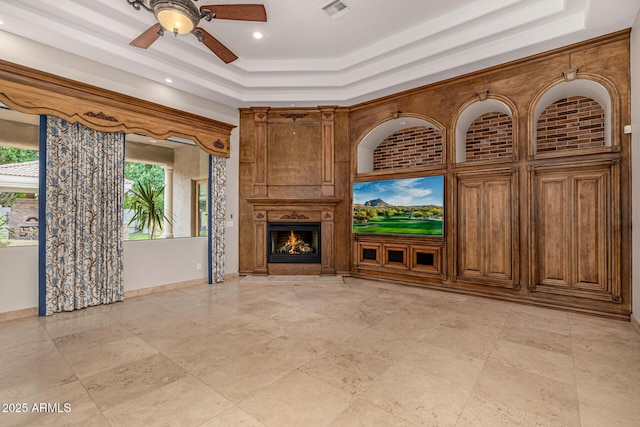 unfurnished living room with ceiling fan, a large fireplace, and a tray ceiling