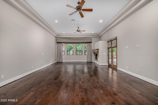 unfurnished living room with ceiling fan, dark wood-type flooring, and a tray ceiling