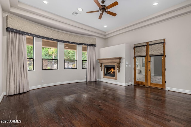 unfurnished living room featuring ceiling fan, a healthy amount of sunlight, dark hardwood / wood-style flooring, and a tray ceiling