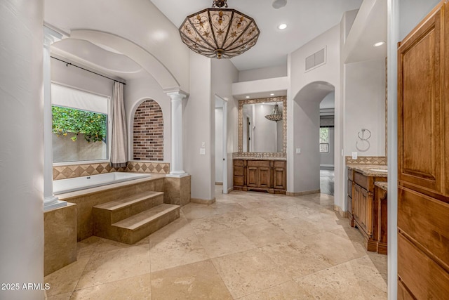 bathroom with decorative columns, plenty of natural light, tiled tub, and vanity