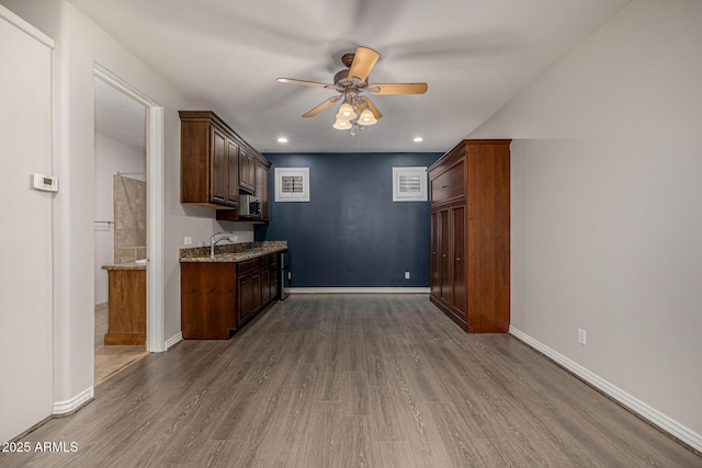 kitchen featuring ceiling fan, sink, light stone counters, and hardwood / wood-style floors