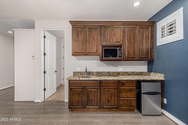 kitchen with stainless steel refrigerator, wood-type flooring, light stone countertops, dark brown cabinetry, and sink