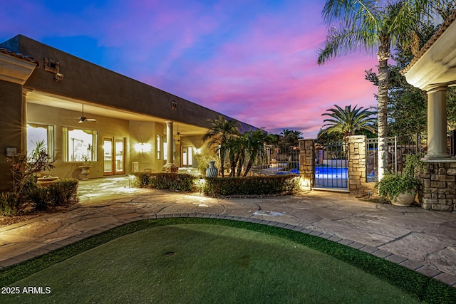 yard at dusk featuring ceiling fan and french doors