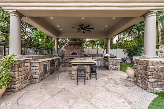 view of patio / terrace with area for grilling, an outdoor brick fireplace, a grill, ceiling fan, and a wet bar